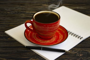 Bir fincan kahve, tahta arka planda kağıt defter.