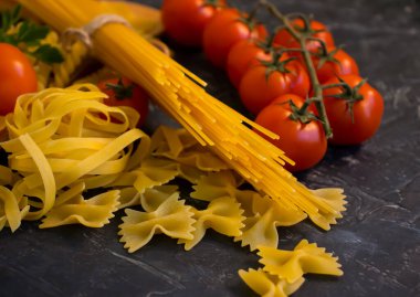 Kuru farklı makarna, beton arkaplanda domates.