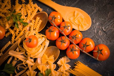 Kuru farklı makarna, beton arkaplanda domates.