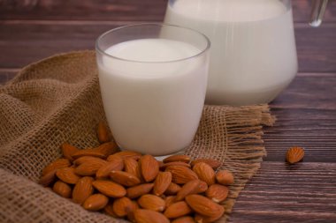 Bir bardak süt, ahşap arka planda badem.