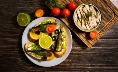 sprats in a can, fresh dill on wooden background