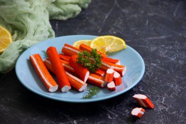 Koyu arkaplanda bir tabakta yengeç çubukları