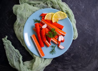 Koyu arkaplanda bir tabakta yengeç çubukları