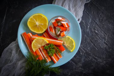 Koyu arkaplanda bir tabakta yengeç çubukları