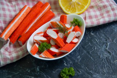 Koyu arkaplanda bir tabakta yengeç çubukları