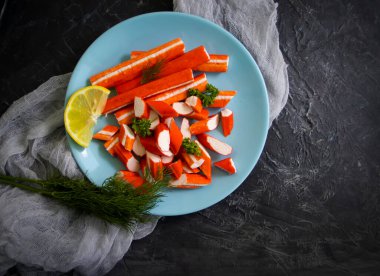 Koyu arkaplanda bir tabakta yengeç çubukları