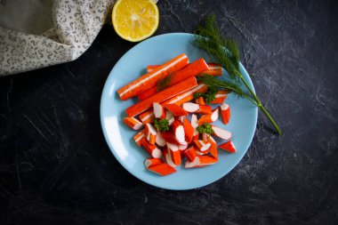 Koyu arkaplanda bir tabakta yengeç çubukları