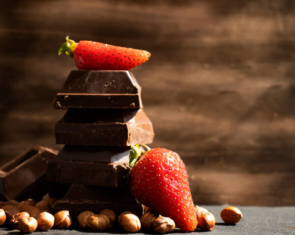 Dark chocolate, fresh strawberries, nuts on a dark background