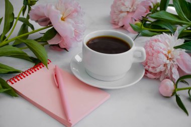 Bir fincan kahve, şakayık çiçeği, arka planda bir defter.