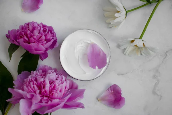 Cosmetic cream, peony flower on a light background, chamomile flower