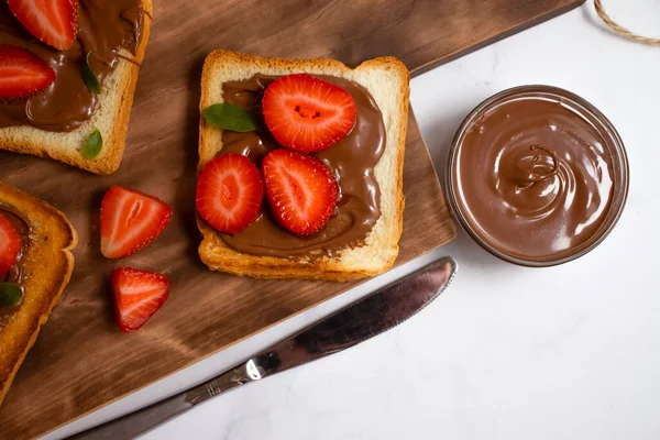 Bread with chocolate paste, strawberries on a light background