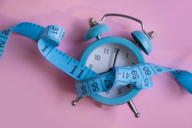 Alarm clock, measuring tape on a colored background