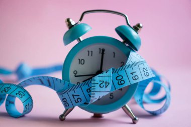 Alarm clock, measuring tape on a colored background