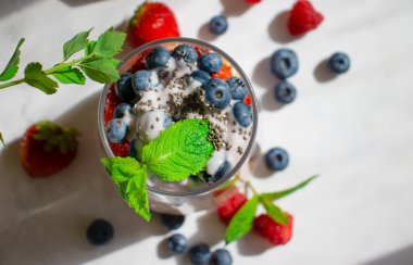 Yogurt, chia seeds, raspberries, strawberries, blueberries, mint on a light background