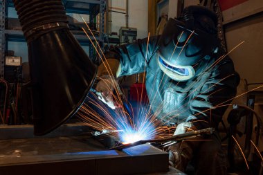 Metal ve kıvılcımlar üreten koruyucu maskeli kaynakçı. Fabrikada endüstriyel çelik kaynakçısı.