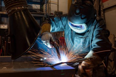 Metal ve kıvılcımlar üreten koruyucu maskeli kaynakçı. Fabrikada endüstriyel çelik kaynakçısı.