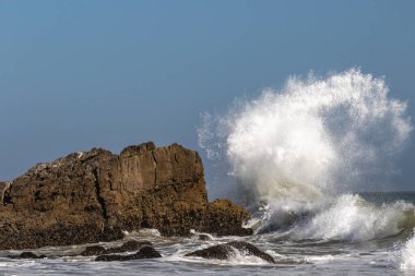 Malibu, California yakınlarındaki kıyı kayalarında büyük dalgalar koparak havaya püskürtülmüş ve geriye doğru kıvrılmıştır. Yakınlarda başka bir dev kaya daha. 