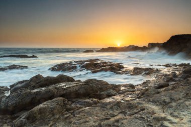 Günbatımı Leo Carrillo plajında, Malibu, California yakınlarında. Ufkun hemen üstündeki turuncu güneş. Rocky plajı ve ipeksi, akan su. Uzakta kayalıklar. 