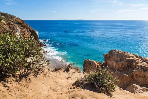 Point Dume, Malibu, California 'daki kayalıklardan görüntü. Bitkiler ve kayalar ön planda. Pasifik Okyanusu, gökyüzü ve uzak bulutlar.  