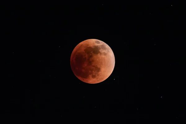 Full moon (blood moon) at the height of a lunar eclipse. Deep red color. Black sky and stars in background.