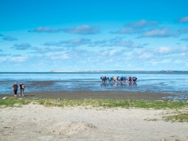 Kuzey Alman Wadden Denizi 'nin alçak akıntılı manzarası. Mavi gökyüzünde, bulutlu, çamurlu, düz bir grup yürüyüşçü rehberlik ediyor.. 