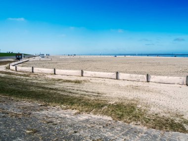 Landscape view of the smoothed bathing beach with fence near Neuharlingersiel in East Friesland in March 2022 with a blue sky and a view to the horizon. clipart