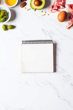 Keto diyet malzemeleri ve beyaz mermer arka plan üzerine kağıt defter, kopyalama alanı. Ketogenik gıda konsepti.