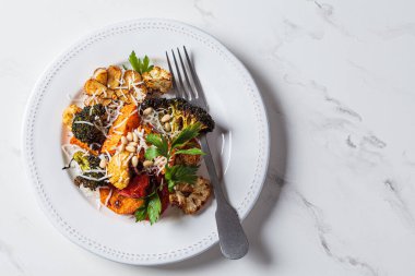 Fırında sebze (brokoli, karnabahar, tatlı patates ve sarımsak) karışımı beyaz tabakta peynir, üst manzara. Vejetaryen sağlıklı detoks yemeği..