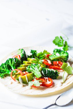 Brokolili vegan tortilla, avokado ve tahini sosu beyaz mermer arka planda. Vejetaryen fast food.