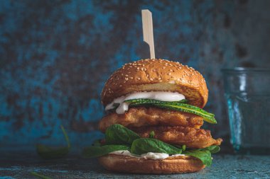 Gri tabakta balık burger, koyu mavi arka plan, kopyalama alanı. Hamurda balık, mayonez ve ıspanaklı sandviç..