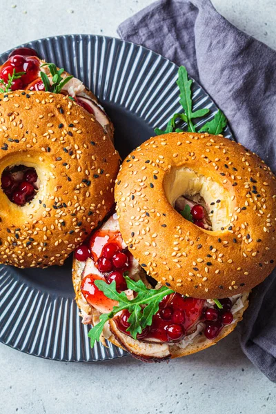 Thanksgiving food concept. Bagel sandwich with turkey and cranberry sauce on gray plate, top view, close-up.