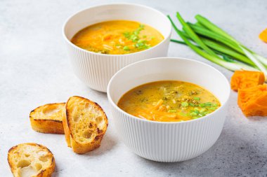 Ev yapımı brokoli çedar peyniri çorbası, beyaz kasede yeşil soğan, gri arka plan. Vejetaryen gıda konsepti.