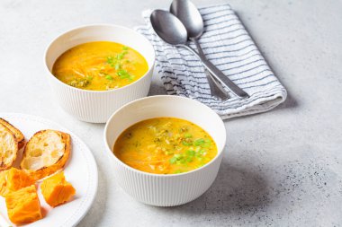 Ev yapımı brokoli çedar peyniri çorbası, beyaz kasede yeşil soğan, gri arka plan. Vejetaryen gıda konsepti.