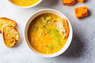 Ev yapımı brokoli çedar peyniri çorbası, beyaz kasede yeşil soğan, gri arka plan, üst manzara. Vejetaryen gıda konsepti.