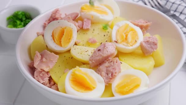 マグロとジャガイモのサラダに卵とネギを白いボウルに入れます。健康的な菜食、フィットネスの食事. — ストック動画