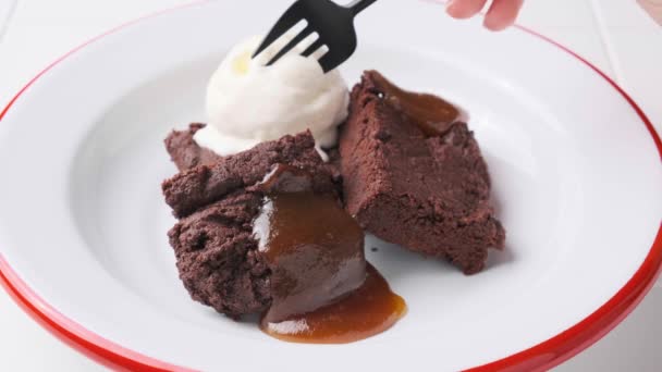 Carrés brownie végétalien avec une cuillère de crème glacée sans produits laitiers et caramel aux pommes dans une assiette blanche. — Video