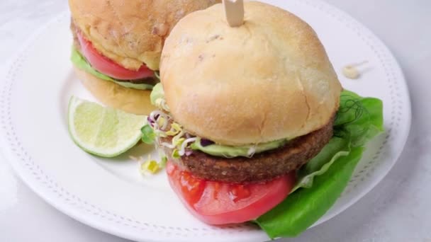 Vegan burger dengan alpukat, tomat dan saus kacang, latar belakang putih, berputar. — Stok Video