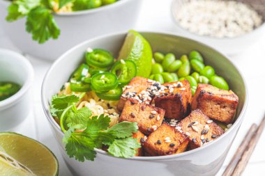 Vejetaryen erişteli ramen çorbası, terbiye edilmiş tofu, edamame fasulyesi ve beyaz fayanslı gri bir kasede acı biber. Yakın plan..