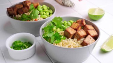 Vejetaryen erişteli ramen çorbası tofu, edamame fasulyesi ve gri kaselerde acı biber..