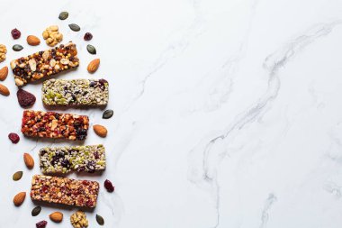 Energy granola bars with different seeds, nuts and dried fruits and berries on a white marble background, top view, copy space. Healthy snack concept.