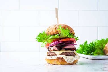 Homemade cheeseburger with bacon, vegetables and sauce, white background, copy space. Homemade fast food concept.