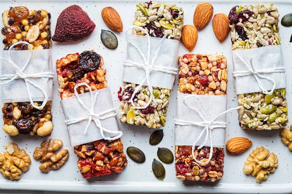 Energy granola bars with different seeds, nuts and dried fruits and berries on a white marble background, top view, close-up. Healthy snack concept.