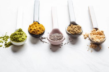 Süper yiyecek tozları kaşıklarda, beyaz mermer arka plan, kopyalama alanı.