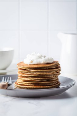 Kremalı krep yığını gri tabakta, beyaz mutfak.