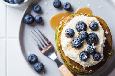 Hindistan cevizi kremalı kibrit çayı yeşil krep, yaban mersini ve akçaağaç şurubu, beyaz arka plan, üst manzara. Vejetaryen tatlı konsepti.