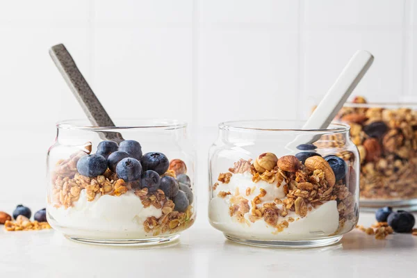 Granola with nuts, yogurt and berries in a jar. Breakfast parfait with muesli, yoghurt and blueberries, white kitchen background.