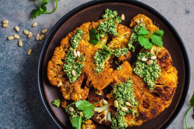 Baharatlı ızgara karnabahar bifteği, ev yapımı yeşil pesto ve koyu bir arka plan..