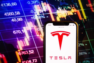KONSKIE, POLAND - August 07, 2022: Smartphone displaying logo of Tesla, Inc American multinational automotive and clean energy company on stock exchange diagram background