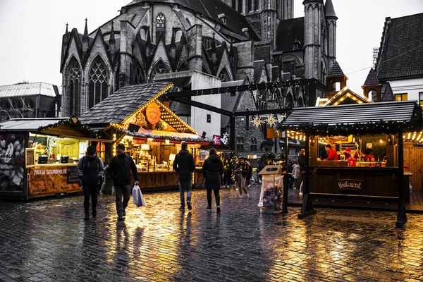 16 Aralık, Gent, Belçika. Eski gotik katedralin yakınında geleneksel Noel pazarı. Parlak sarı ışıklar. 