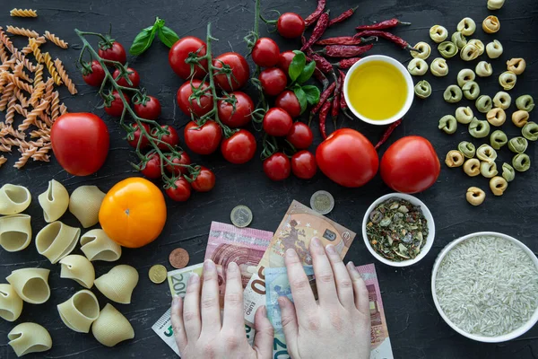 Economical crisis and high costs of daily expenses. Italian pasta and euro banlnotes hold by female hands, top view.